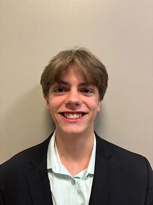 White man with light brown hair wearing a light green dress shirt and black suit jacket